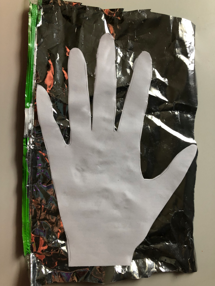 A cut out of white printer paper in the shape of a hand, lying on a piece of mylar. 