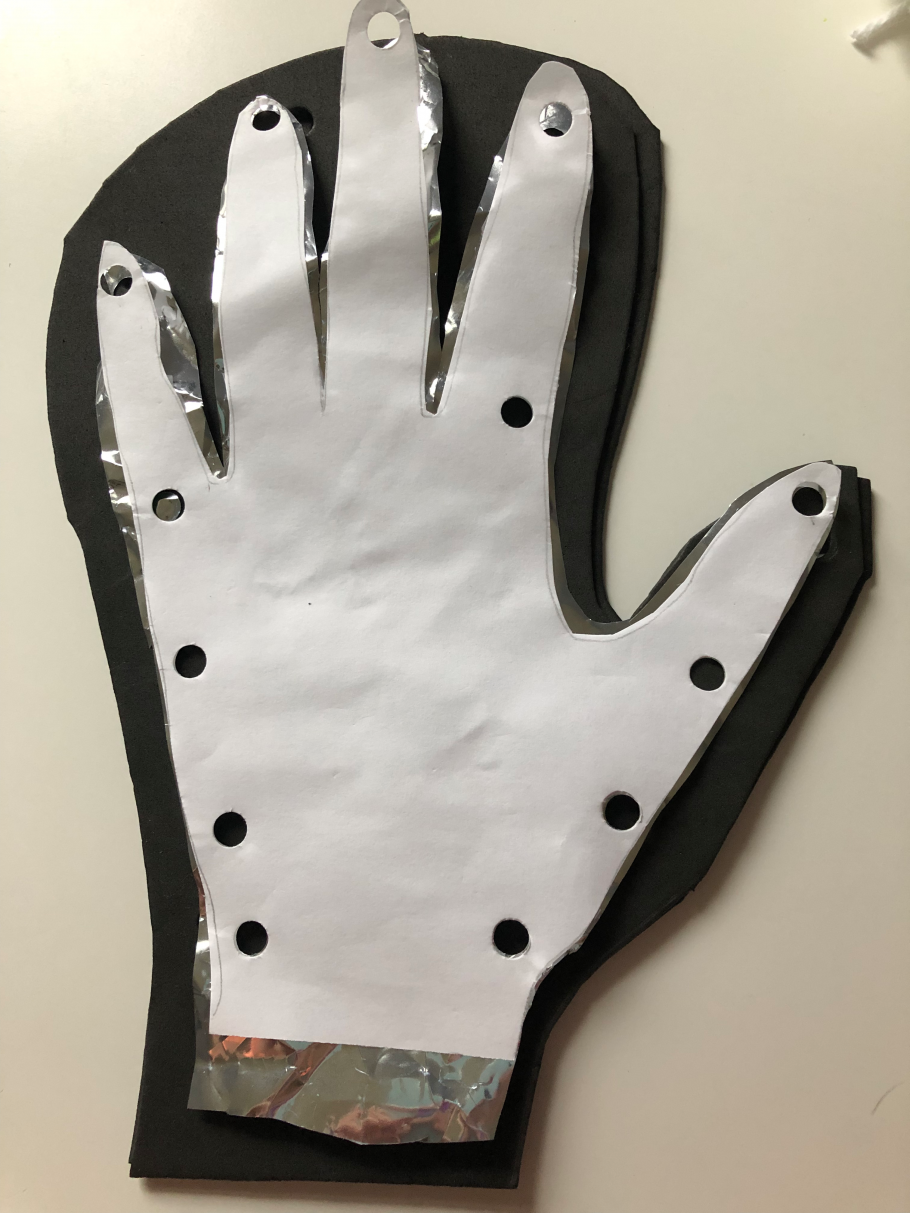 A cut out of a hand on printer paper with hole-punches around the edges, stacked on top of a cut out of a hand on Mylar, stacked on top of a glove shaped cut out on black foam. 