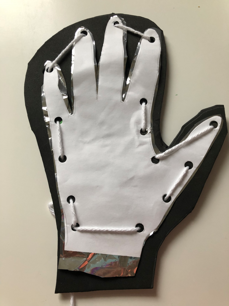 A cut out of a hand on printer paper with hole punches around the outside and yarn threaded through the holes, stacked on top of a cut out of a hand on Mylar, stacked on top of a cut out of a glove on foam. 