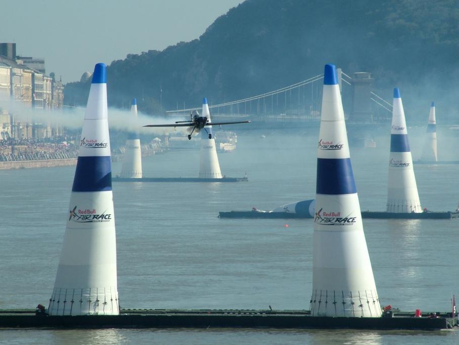 A monoplane flies through a group of pylons positioned on the water.