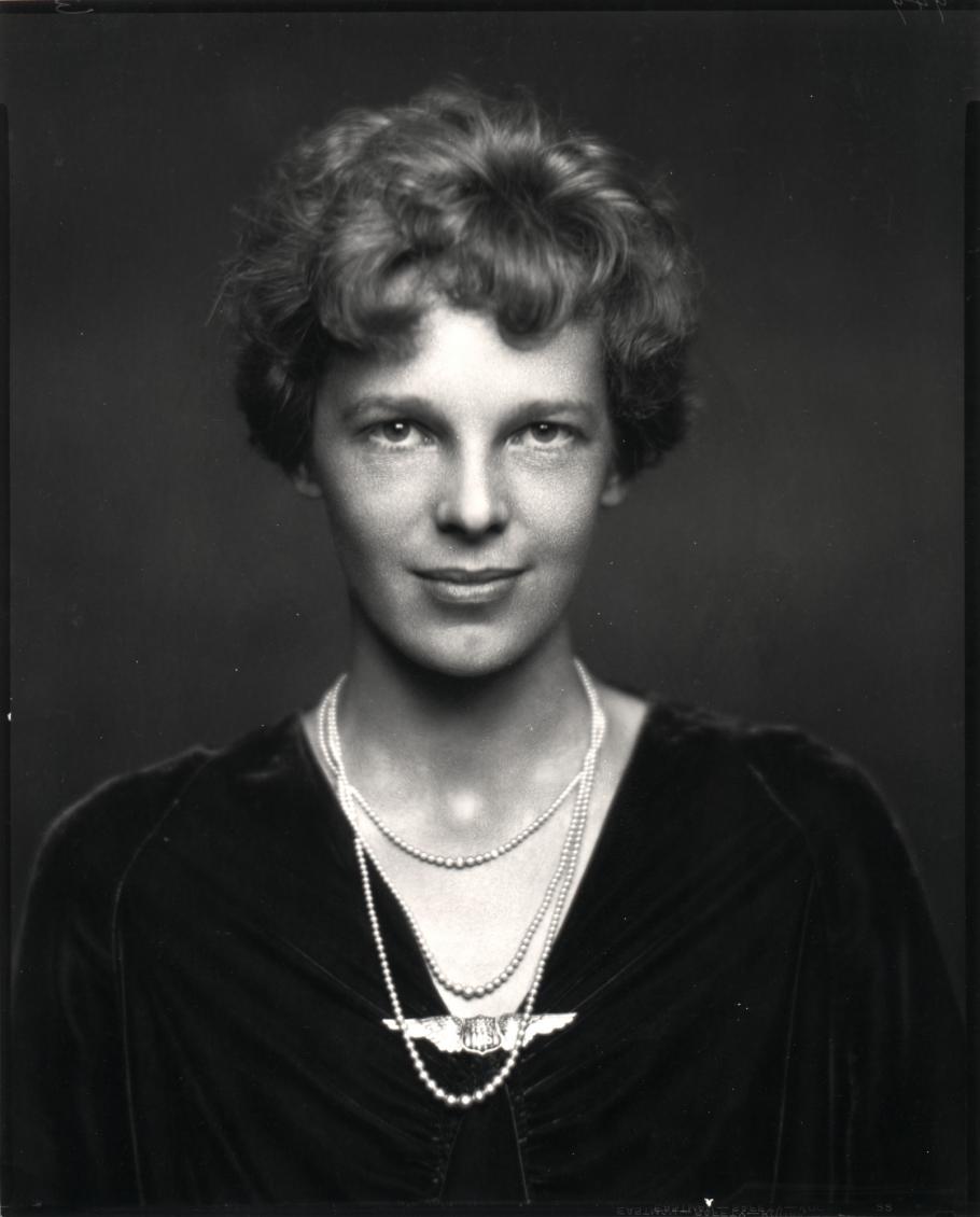 A half body portrait shot of a woman with short hair. One of her necklace has a pendant that looks like wings.