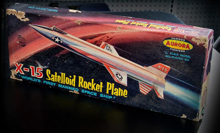 A plastic model airplane kit sits on a table, with artwork on the box depicting an X-15 rocket plane flying into Earth’s orbit.