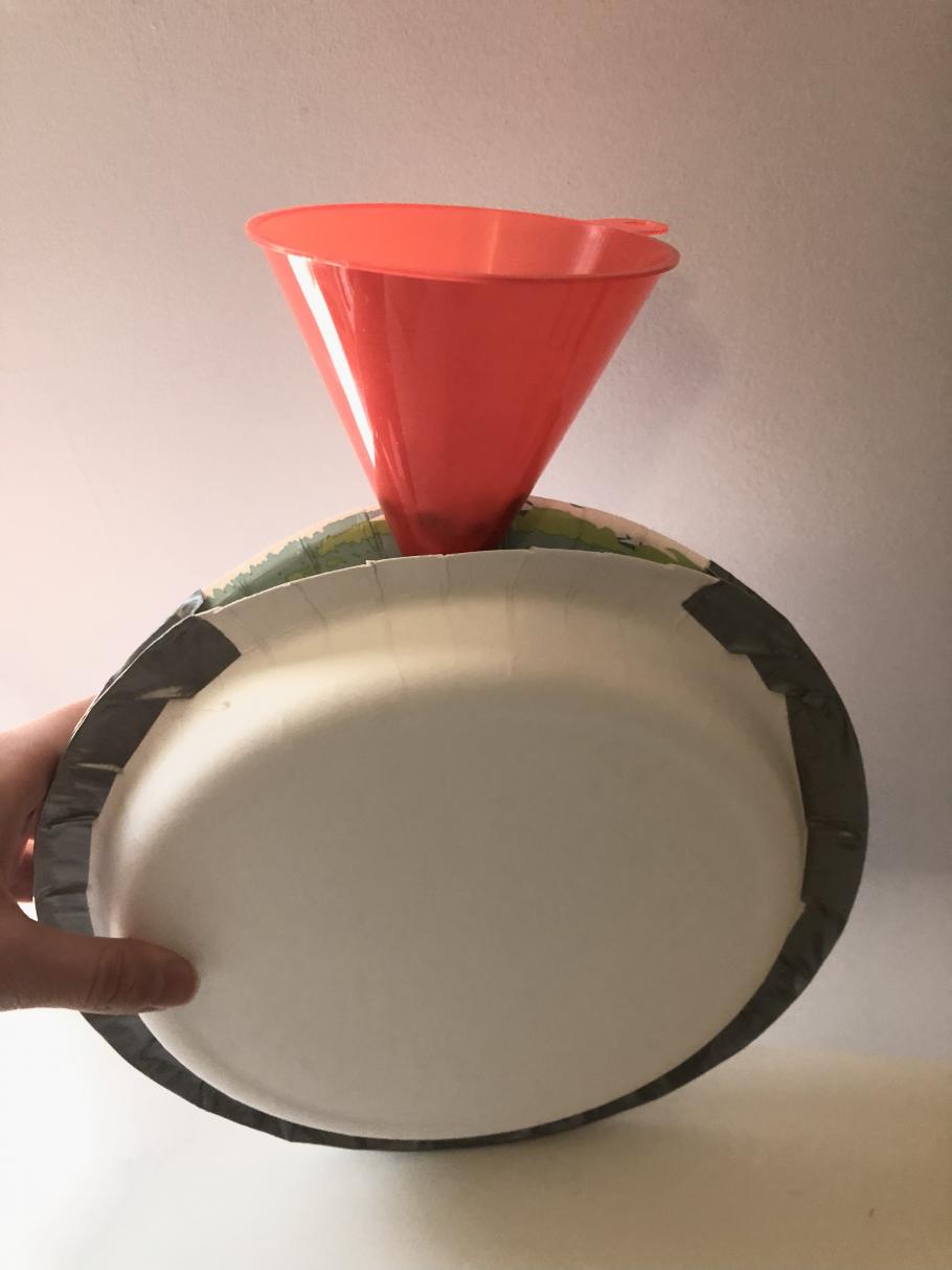 A funnel is inserted in an opening of two plates taped together with duct tape.