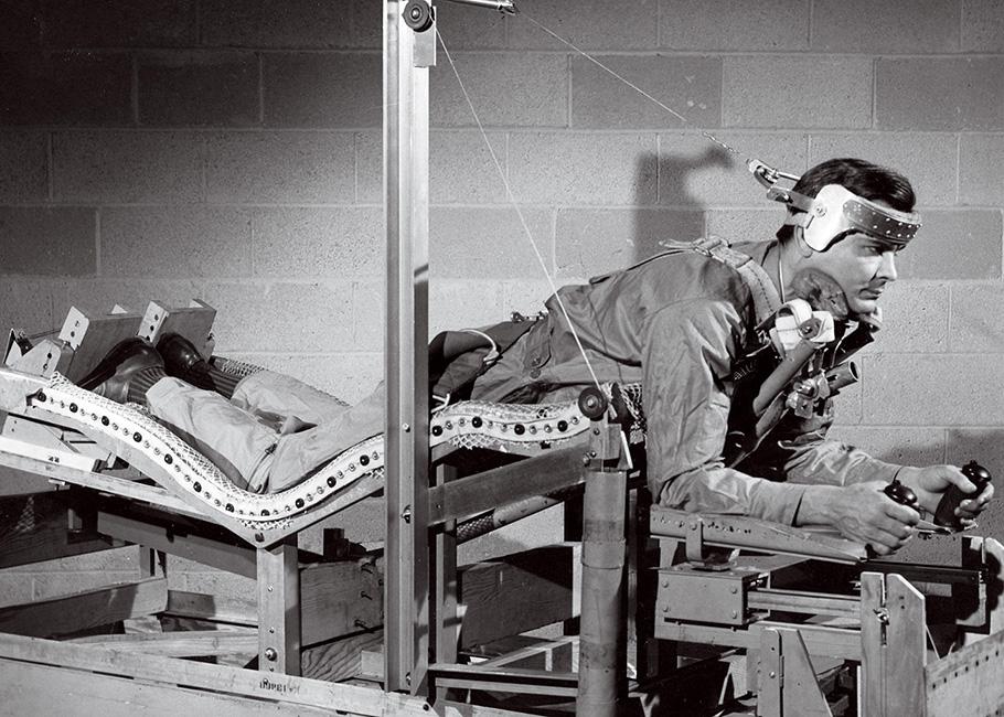 In 1949, an Air Force researcher tests a new design for a pilot’s bed, wearing a metal cap attached by tether to a contraption resembling home fitness equipment.