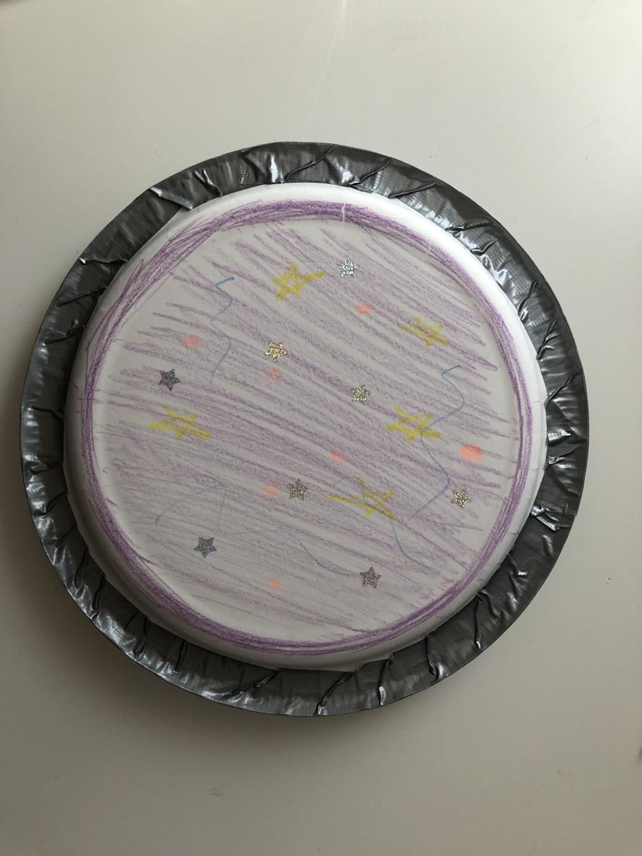 Two plates facing each other taped together with duct tape. The outside of the plate is decorated with stars and purple coloring. 
