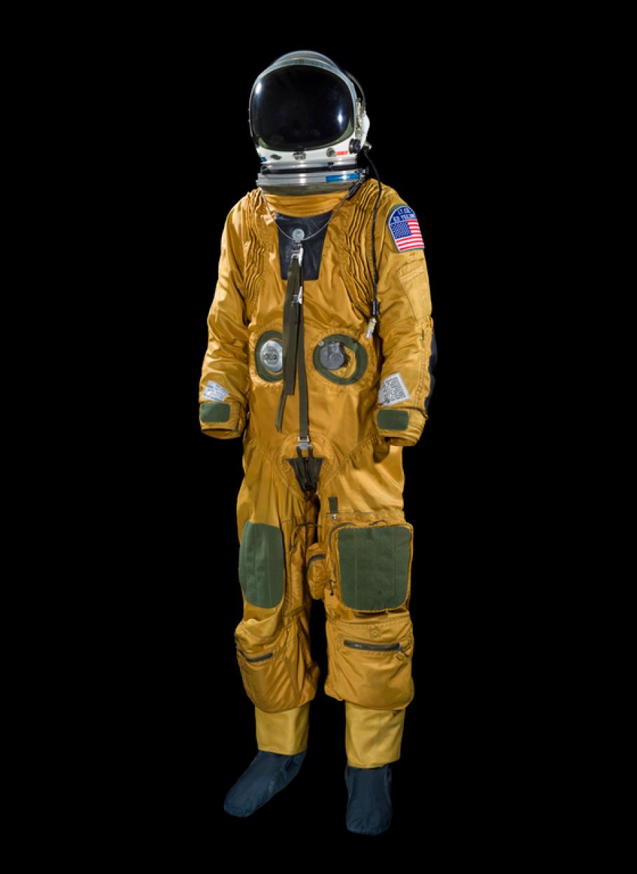 A orange colored full body suit with a helmet attached against a black background.