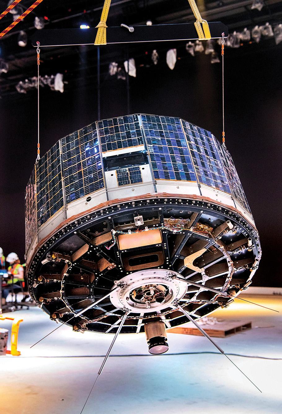 Satellite lifted by two wires attached to crane in gallery under construction.