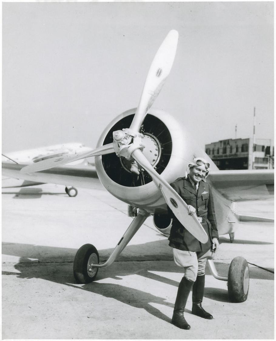 View of the Turner-Laird LTR-14 "Pesco Special" on the ground; pilot Roscoe Turner, in uniform, poses standing behind one blade of propeller at left side of nose of the aircraft.