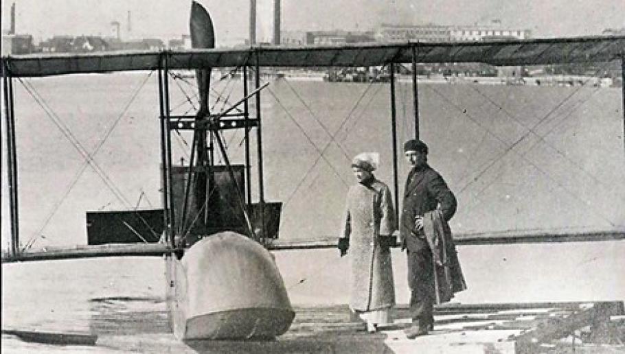A black and white image of two people standing by an aircraft. 