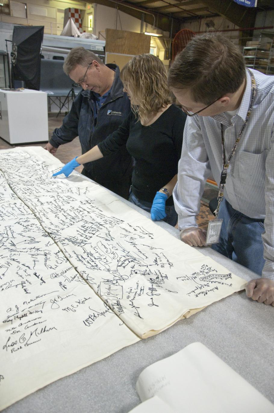 A group of people look at a signed tablecloth. 