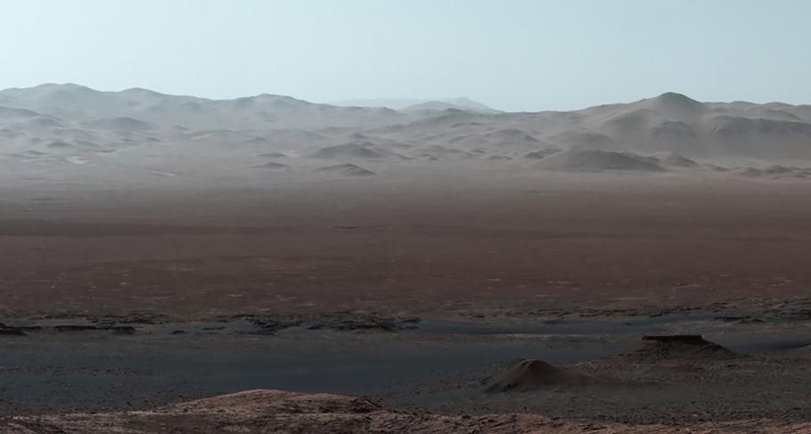 A landscape. In the foreground, is a flat-ish red dusty landscape, in the back is beige hills or mountains.