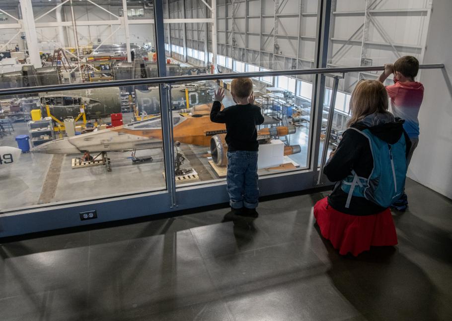 Three visitors look at the X-wing through the windows on the second floor over the Restoration Hangar.