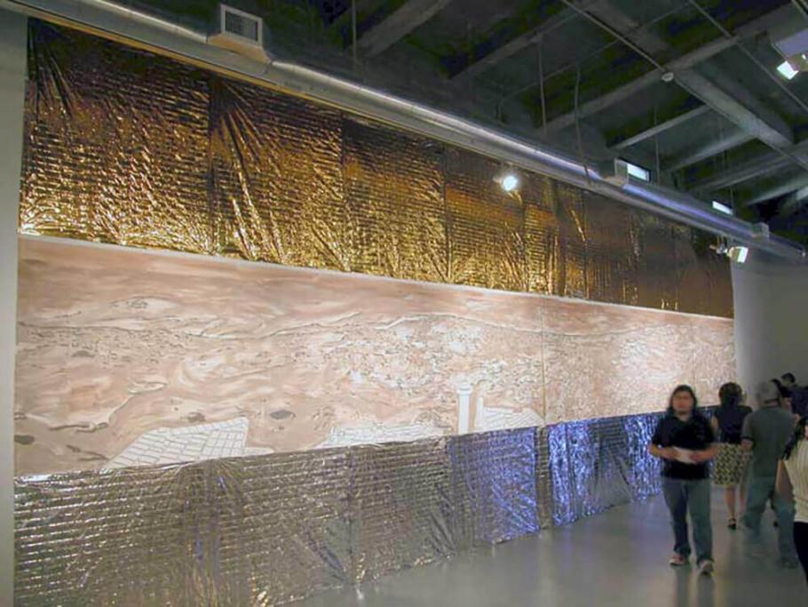 An artwork that consist of gold sheets hanging from a wall in a museum setting as onlookers pass by