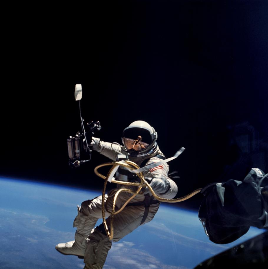 An astronaut floating in space. The Earth can be seen below in the bottom half of the frame. The astronaut holds out a long metal rod in one hand.