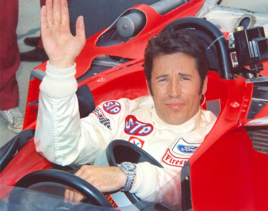 Mario Andretti in the driver's seat of a red race car.