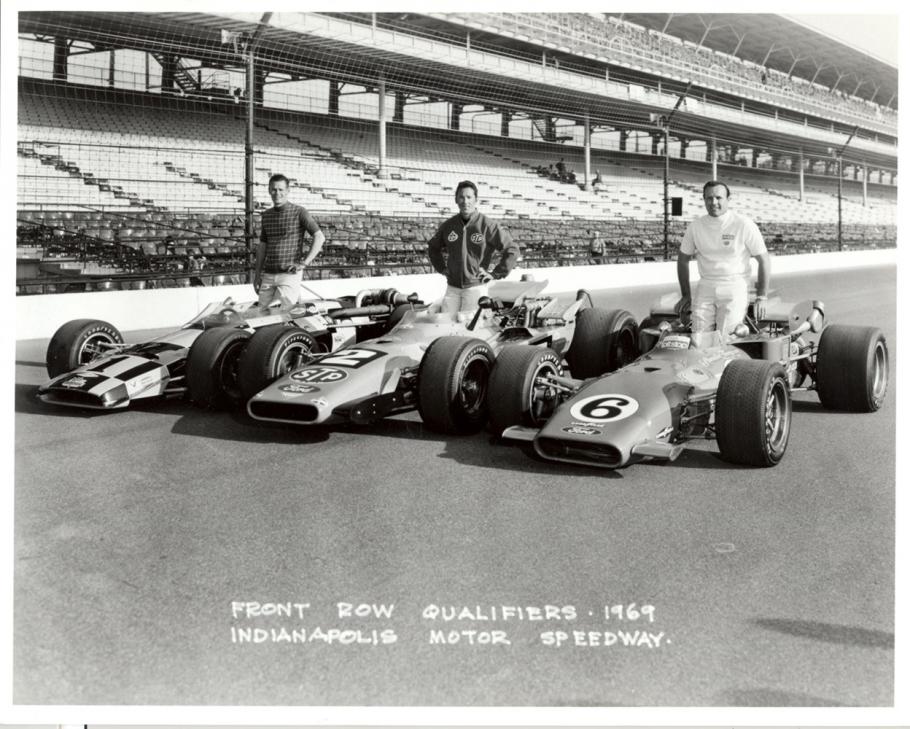 Three men standing behind their Indy 500 race cars.