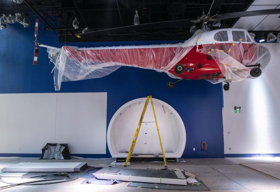 Red helicopter hanging in a nearly-empty gallery while covered in a light sheet of plastic.