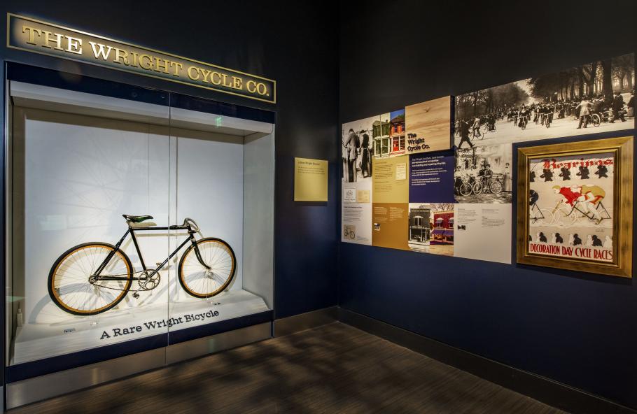 Bicycle in a case that reads "A Rare Wright Bicycle." On the wall next to it are photos and text panels.
