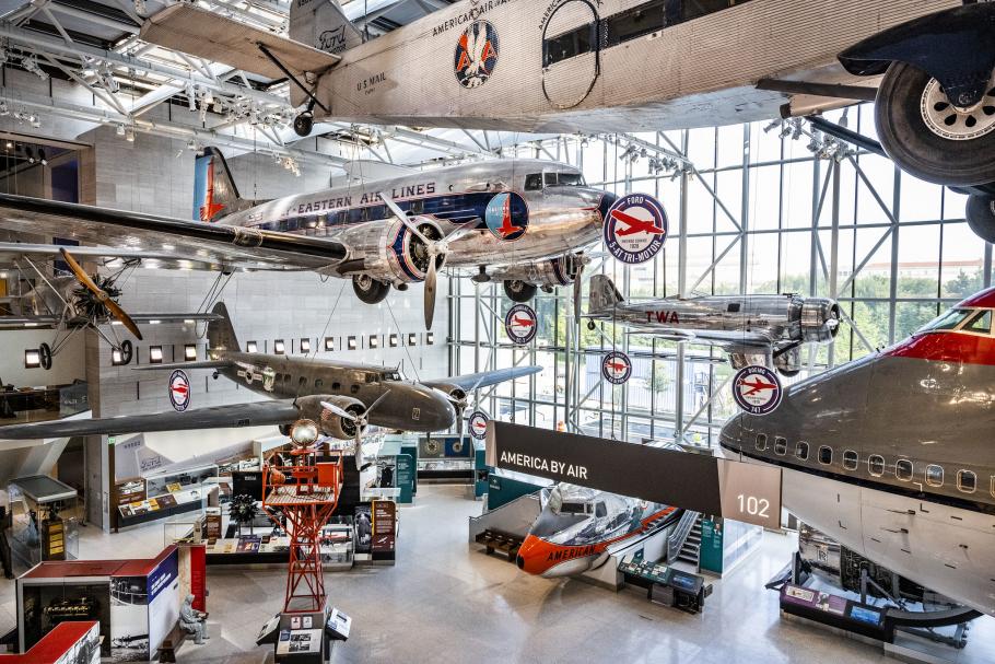 A view of the America by Air gallery. Several large airplanes are suspended from the ceiling with smaller airplanes on the ground. 