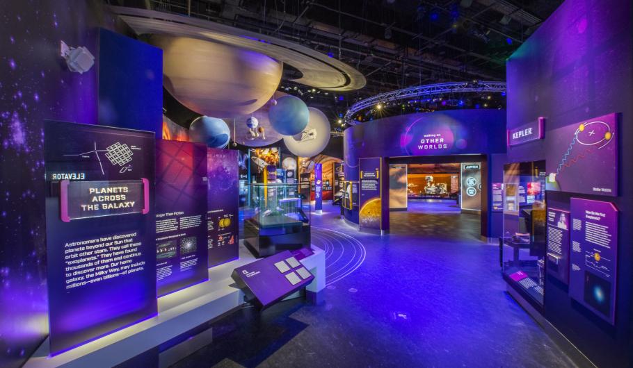 A view of the Kenneth C. Griffin Exploring the Planets Gallery. The overwhelming color of the gallery is purple. There is a model of a solar system hanging from the ceiling, with signage on the walls. 