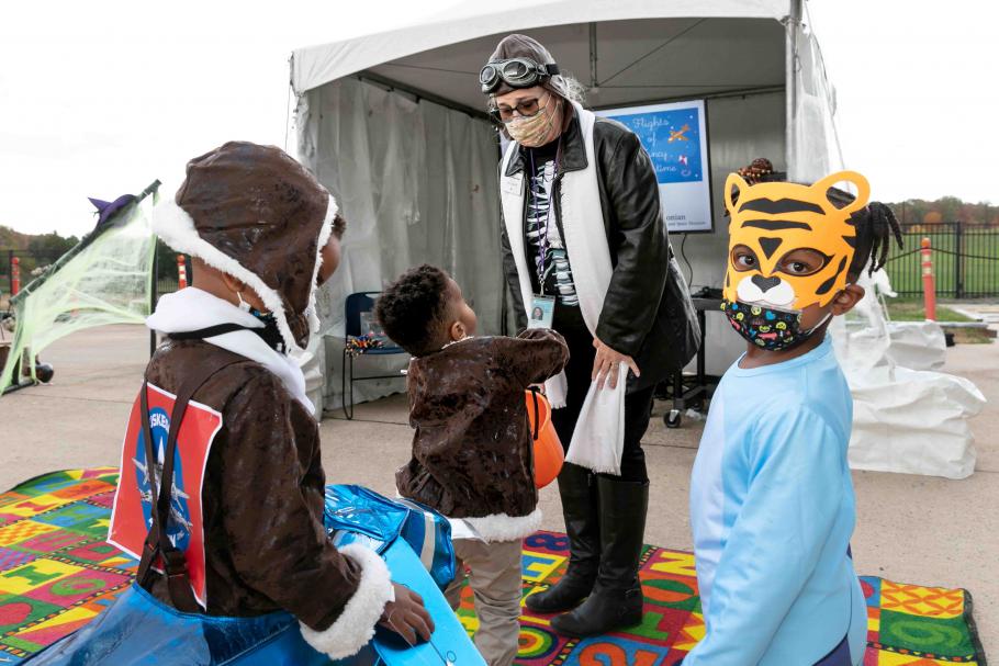 Woman wearing an educator custom gives candy to three young visitors also wearing costumes