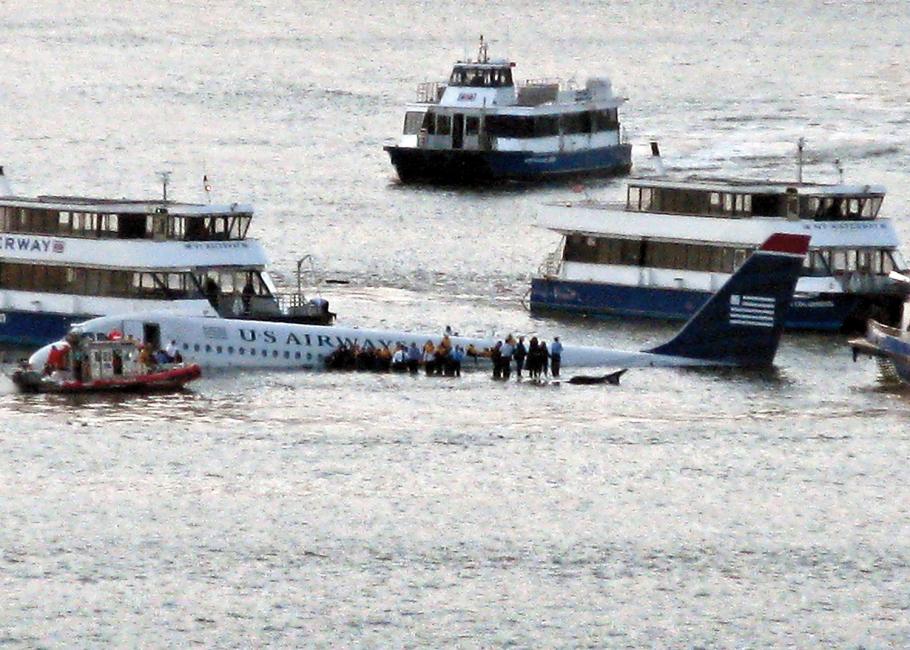 U.S. Airways Flight 1549 floats on the Hudson River with passengers and crew standing on its wing, waiting to be resued by nearby boats.