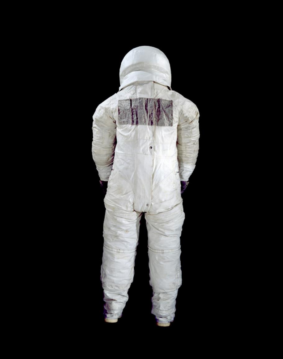 The back of a spacesuit is photographed against a black backdrop