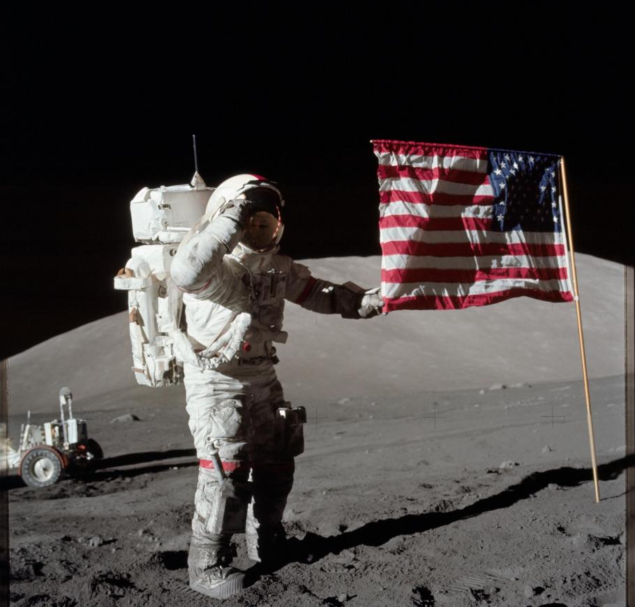 An astronaut stands on the surface of the Moon while touching the American flag