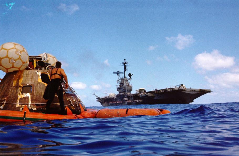 A capsule on a inflated floating device is seen in the ocean and a large ship in the background.