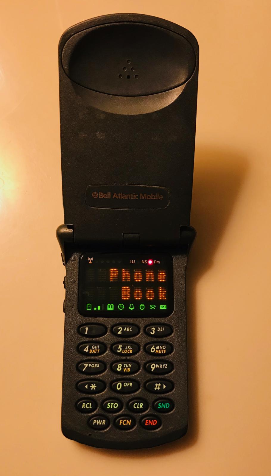A black flip phone, with a small display screen that read "Phone Book"