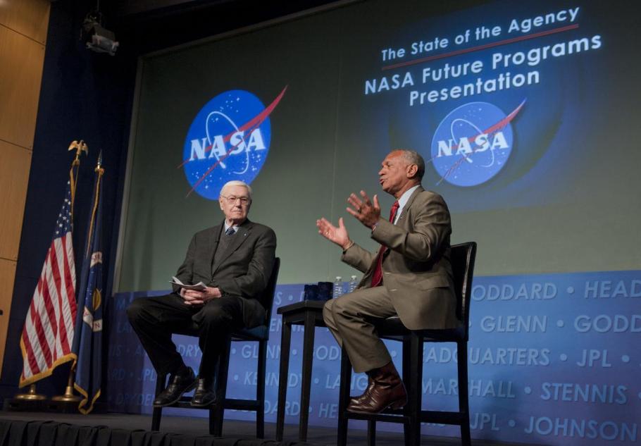 Two men seated on a stage in discussion. The NASA logo is in the background.