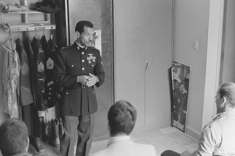 A man in formal military attire speaks to a group of people.
