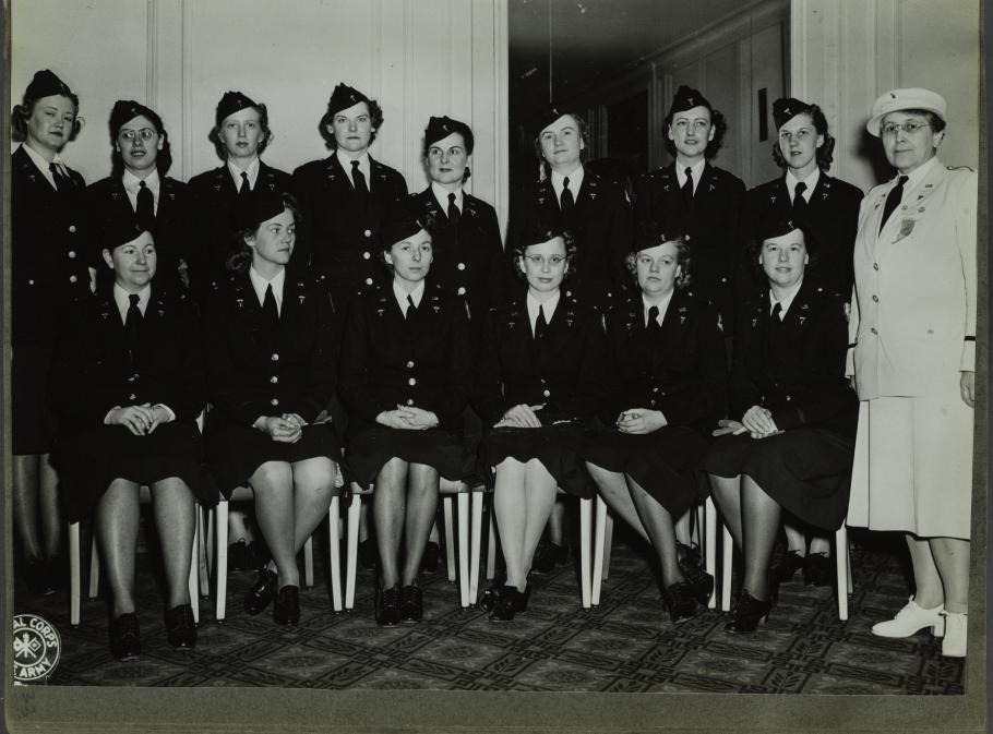 Group photograph of women in dark army uniforms. Eight standing behind six seated with a woman in a white uniform on their left.