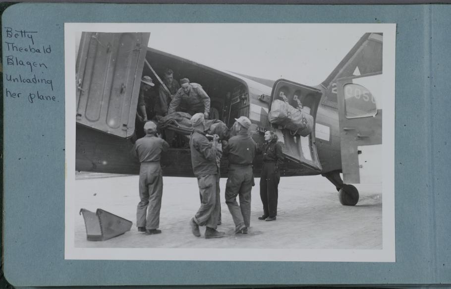 Black and white image of men and women in uniform offloading materials from a plane.