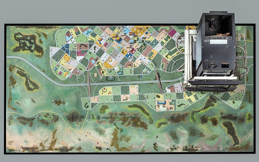Small fake forests and tiny houses are displayed on a panel that looks like it could be part of a model train set. This is actually simulated terrain that helped train fighter pilots.