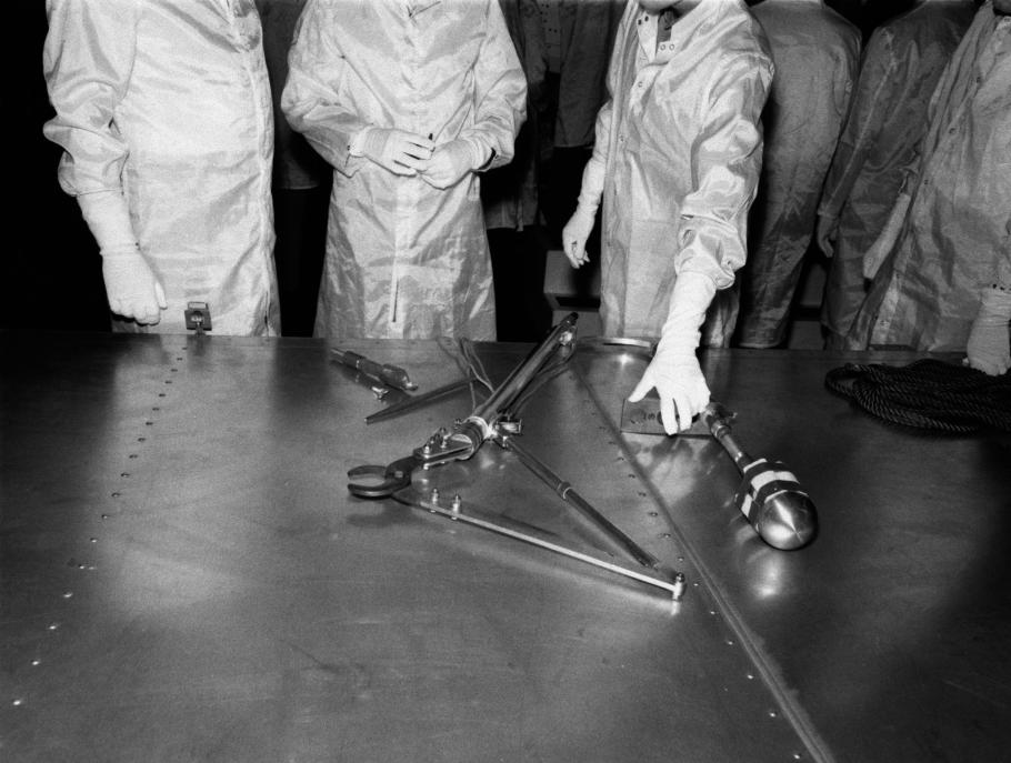 Black and white image of people in lab coats examining tools on a table.