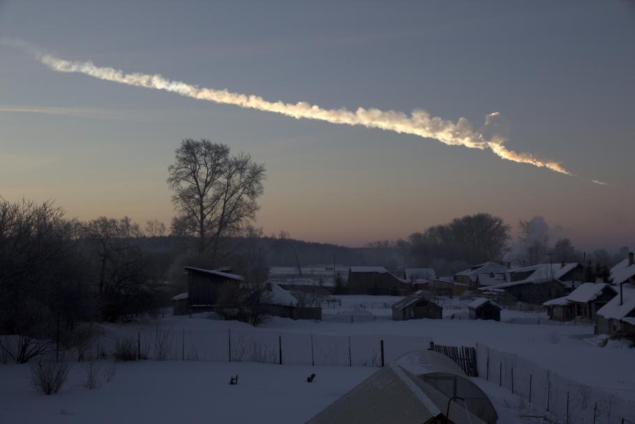 A photograph of a streak of vapor in the sky over a snowy village. 