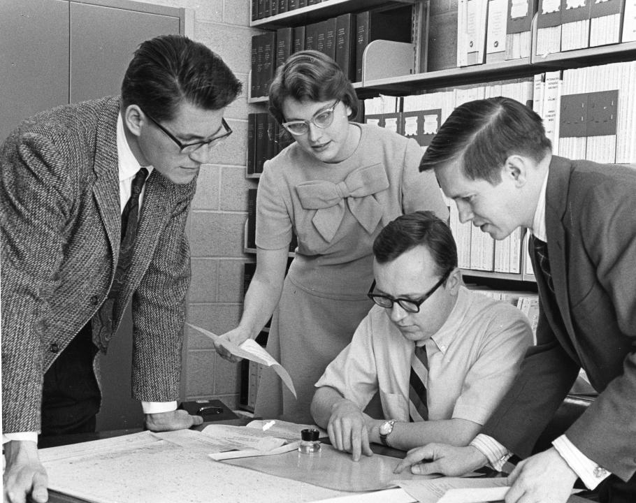 Three men and a woman are looking at a document on a table.