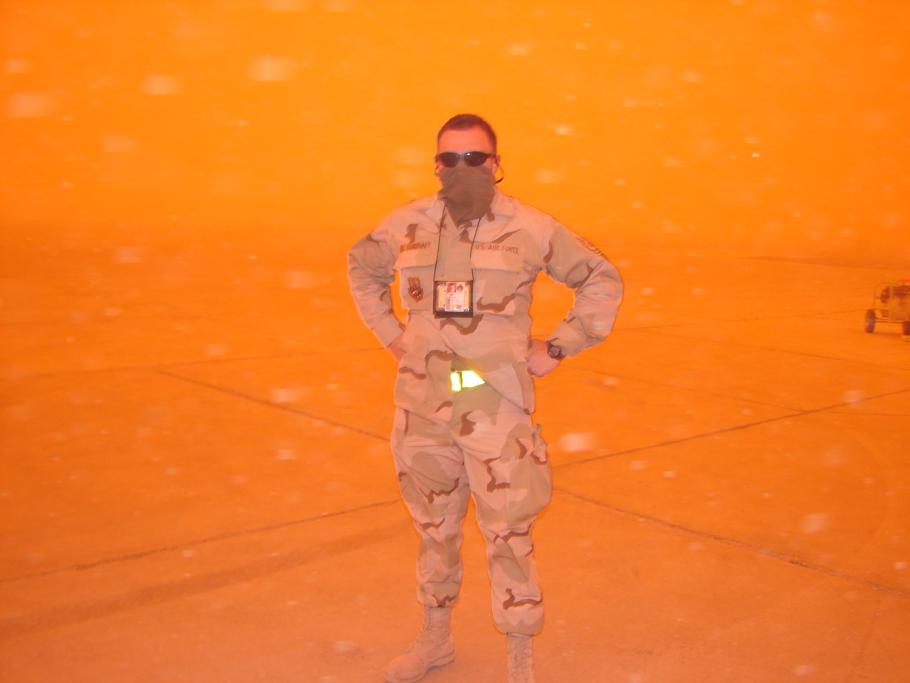 A man in military uniform stands in a sandstorm.