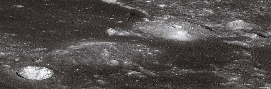 The lunar surface is almost entirely black except for a nearby large crater that is bright white and two grey mounds.