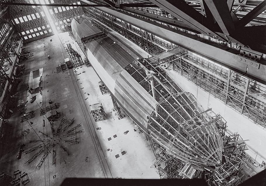 A black and white photo, taken from above. Half the airship is covered with silver-colored cloth while the other half reveals internal struts and girders.