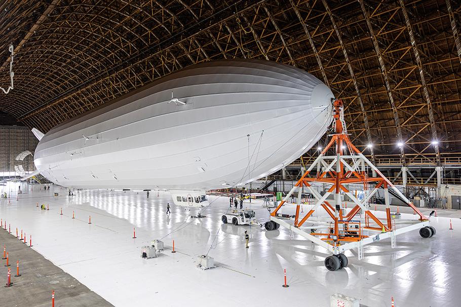 An enormous white airship with no markings is held in place by orange and white scaffolding.