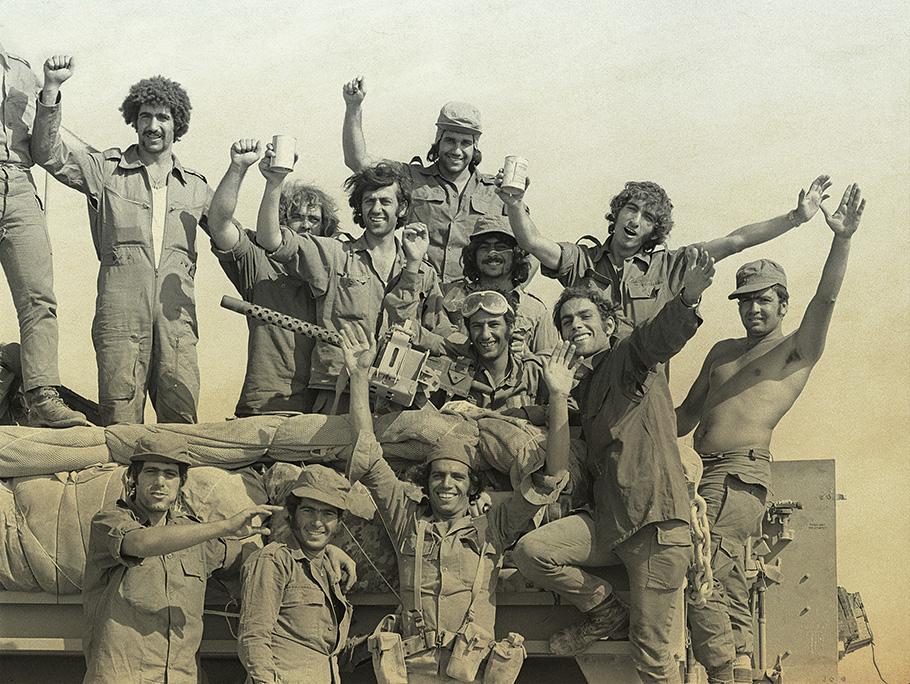 A black and white photo shows a dozen, bedraggled Israeli soldiers, smiling, and with arms raised in apparent celebration.