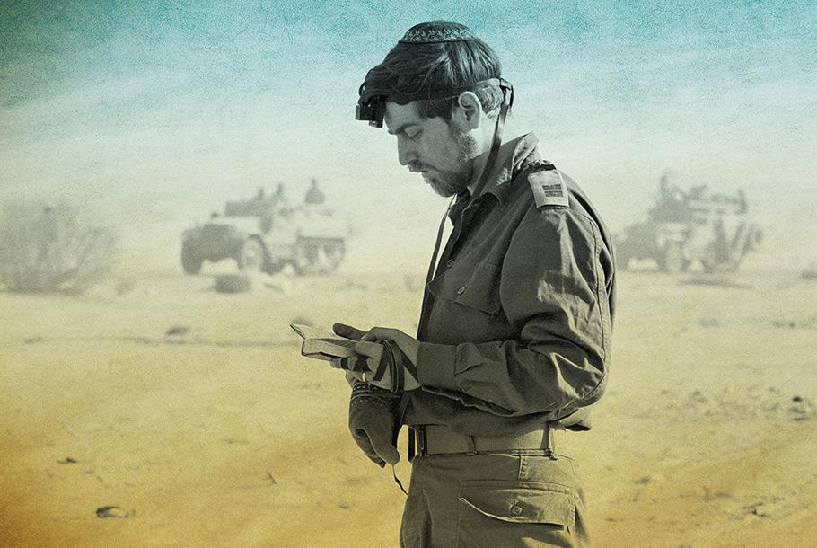 In this colorized photo, an Israeli soldier is praying in the desert while wearing Tefillin. Military vehicles can be seen in the background.