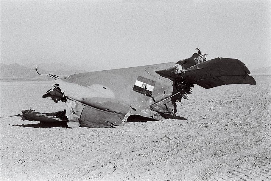 In this black and white photo, the torn piece of an aircraft's tail wing, bearing the Egyptian flag, is partly buried in desert sands.