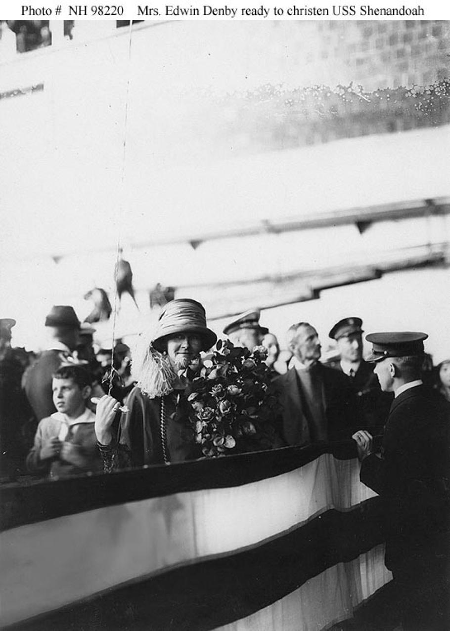 A woman stands facing the camera with a bouquet in her hands as people mill about behind her.