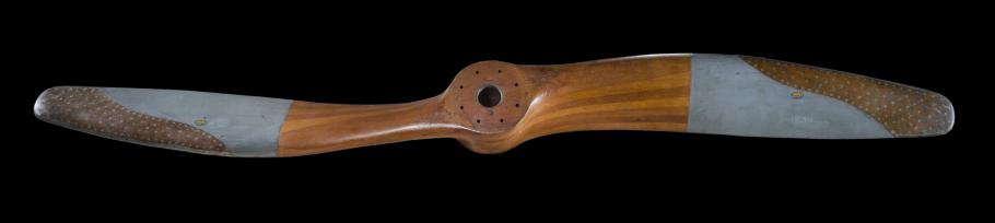 A wooden propeller is photographed against an all black backdrop.