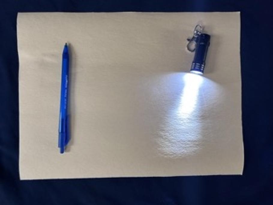 A flashlight and pen sit on a piece of paper. 