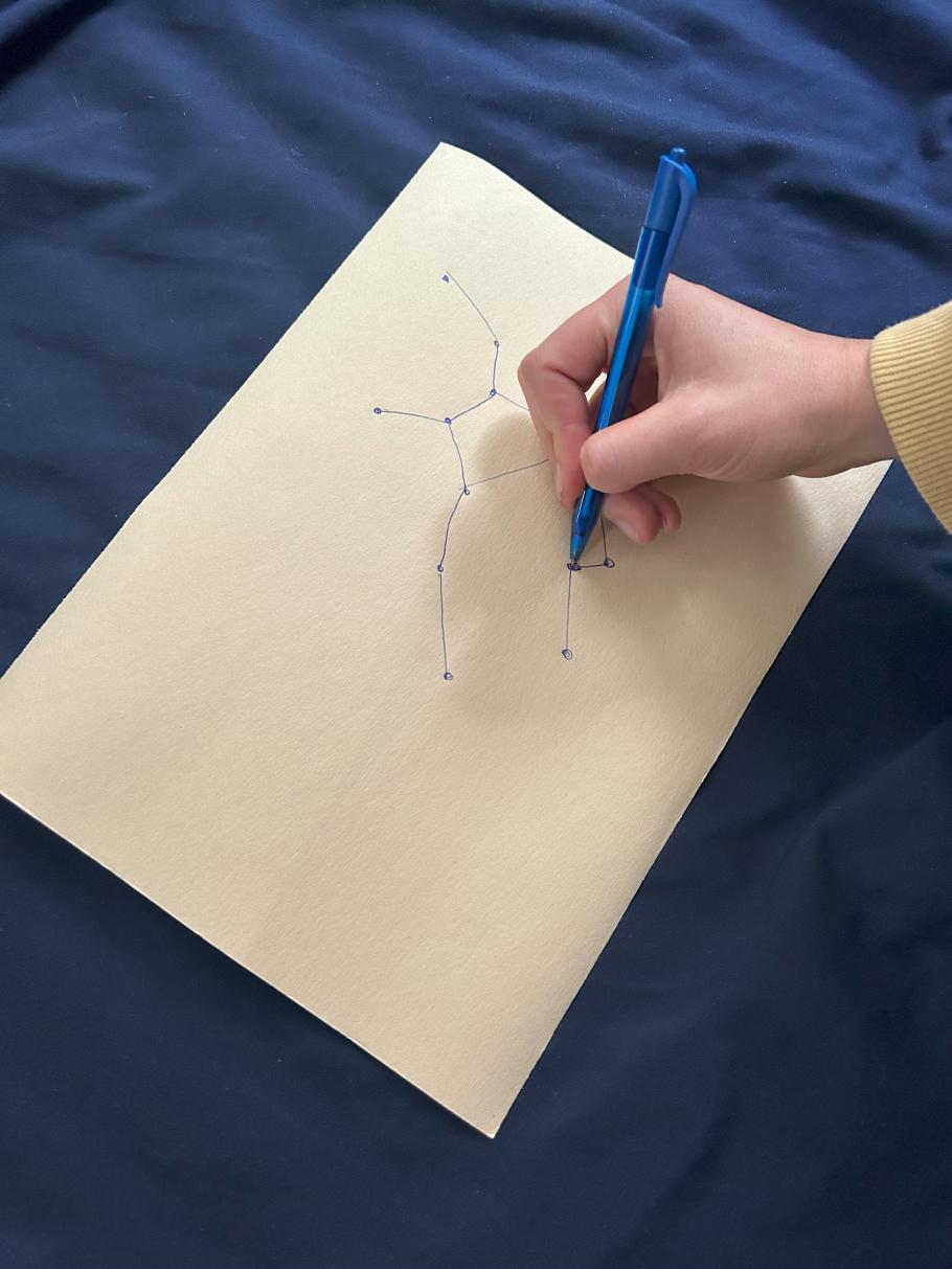 A hand draws a constellation on a piece of paper. 