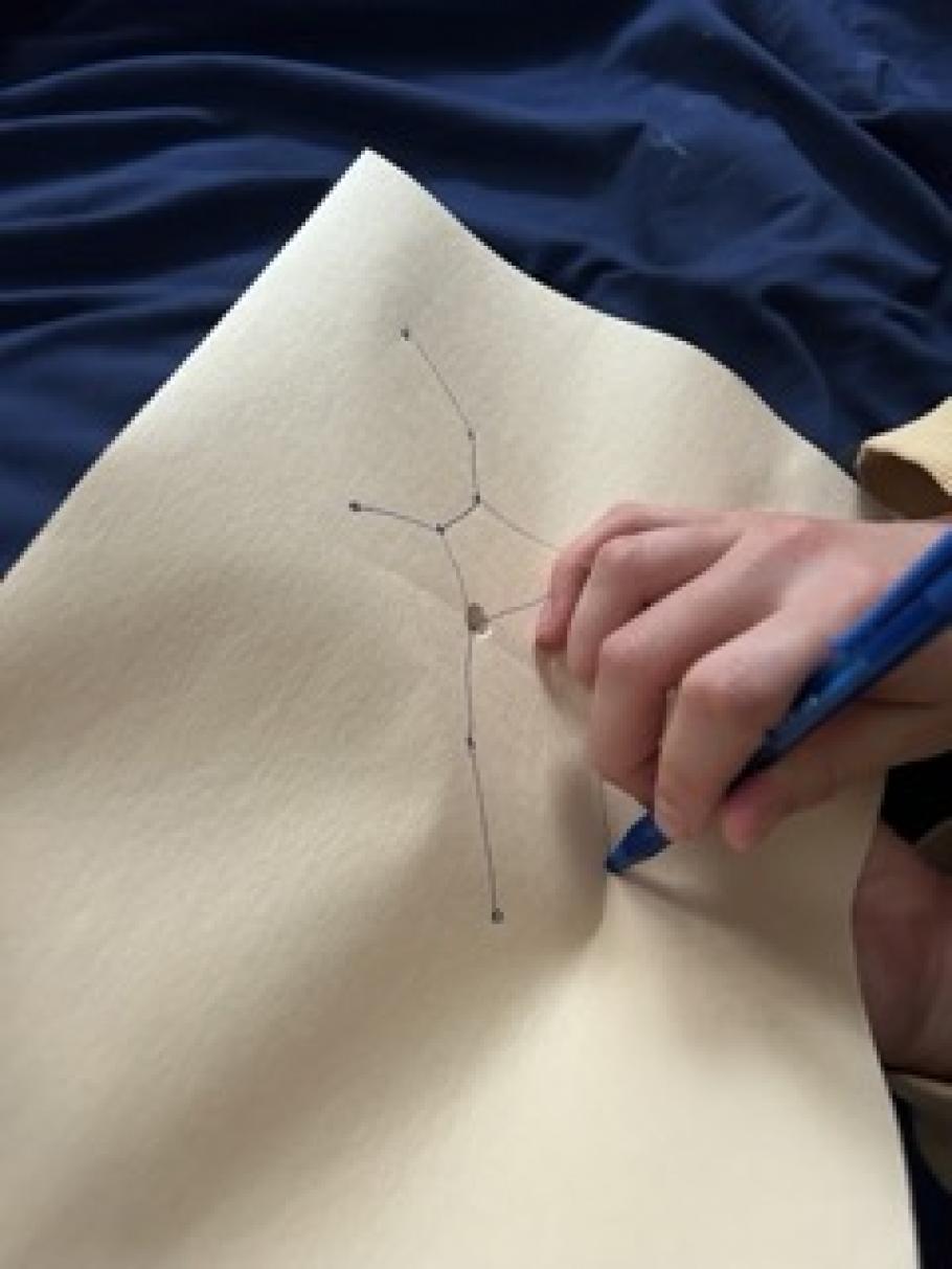 A hand punches holes into a constellation drawn on a piece of paper.